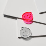 acrylic smiley shapes neon yellow, mirror silver and pink laying on a neutral white background